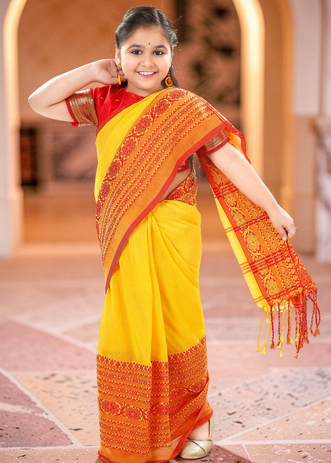 Young girl smiling in a vibrant yellow and red pure cotton handloom saree, perfect for kids ethnic wear during Durga Puja or weddings